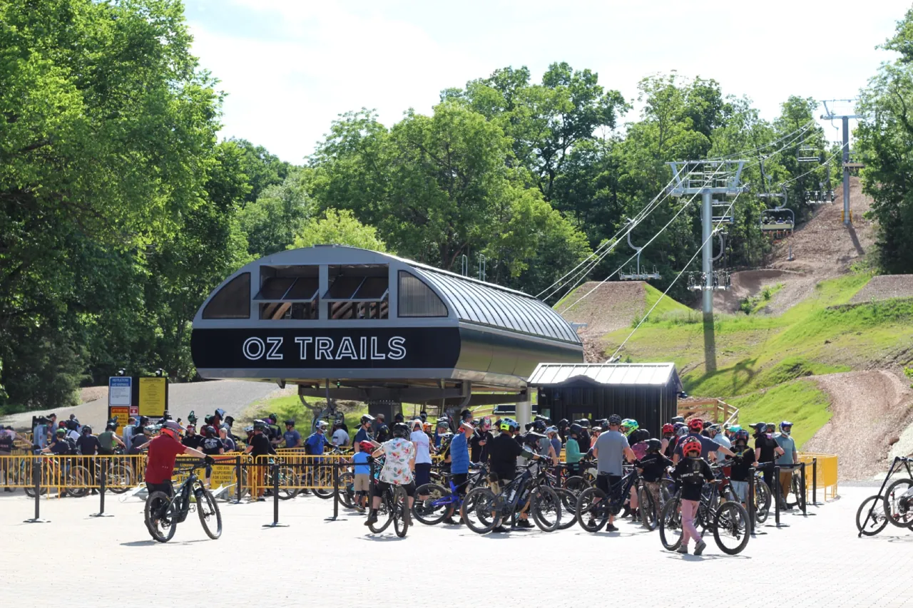 Riders and a chairlift against the wooded hillside at OZ Trails Bike Park in Bella Vista